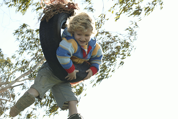 Boy swinging fast on a tire swing on a farm.